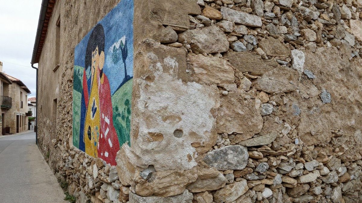 Imagen ilustrativa: detalle de una pared de piedra con un mural colorido en una calle de un pueblo
