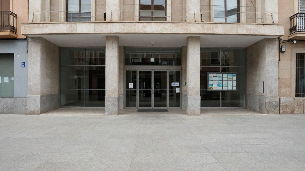 Imagen ilustrativa: entrada de un edificio municipal con tablón de anuncios en un día nublado
