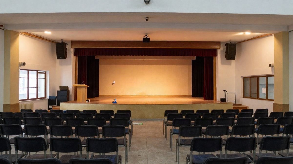 Imagen ilustrativa: interior de un centro cultural con un escenario vacío y sillas en fila, iluminado por luz lateral de ventanas.