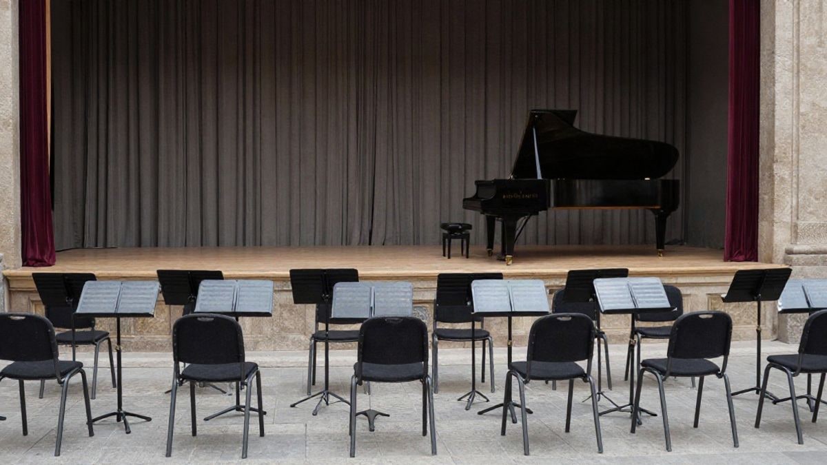 Imagen ilustrativa: escenario vacío de un auditorio municipal con atriles y un piano antes de un concierto