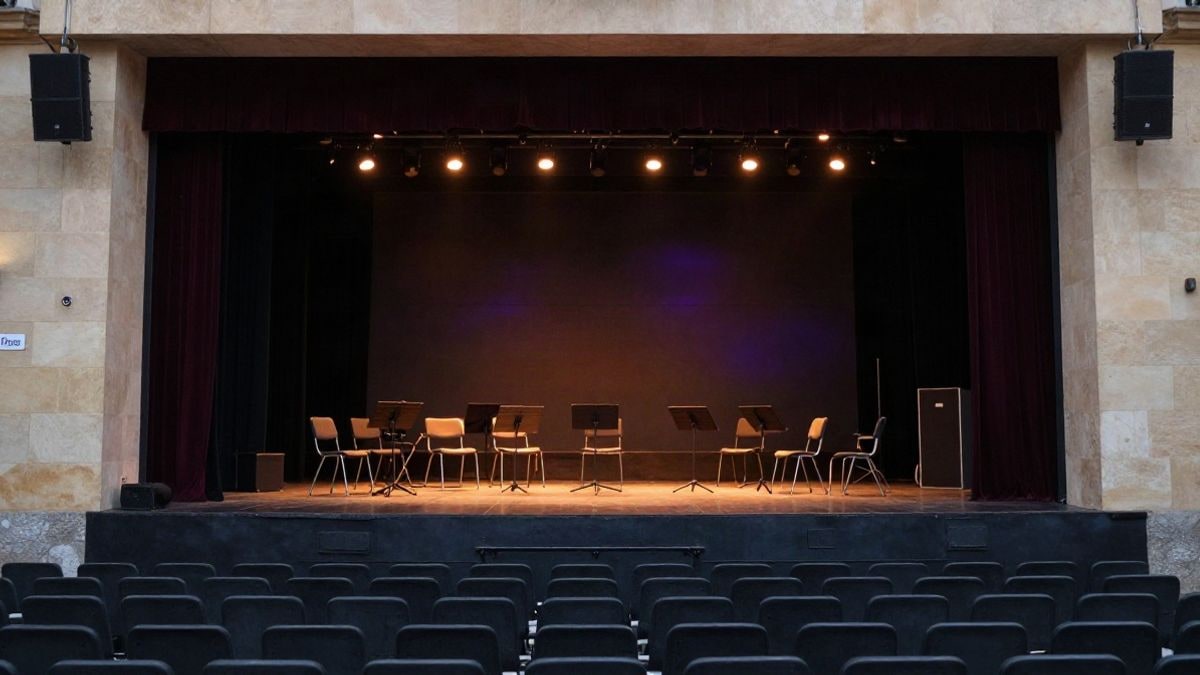 Imagen ilustrativa: un escenario de concierto vacío con atriles y sillas, iluminado con luces cálidas y un ambiente tenue y misterioso