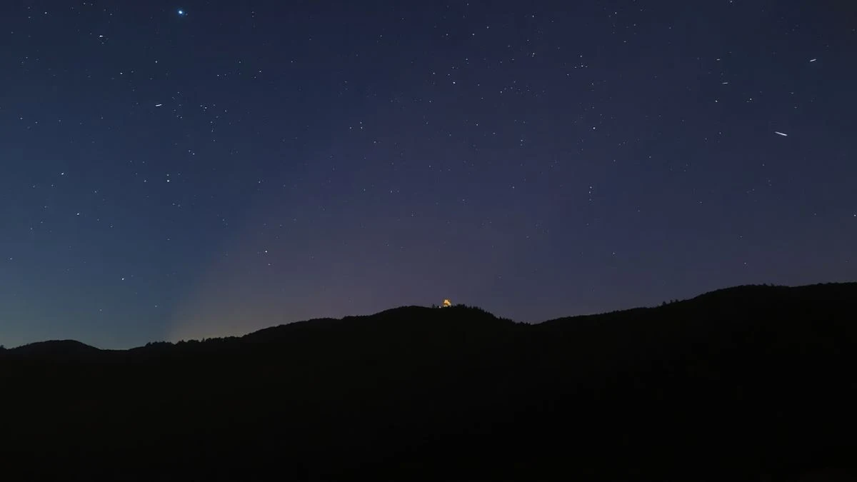 Imagen ilustrativa: cielo nocturno estrellado sobre un paisaje montañoso oscuro, con alguna estrella fugaz y un horizonte lejano.