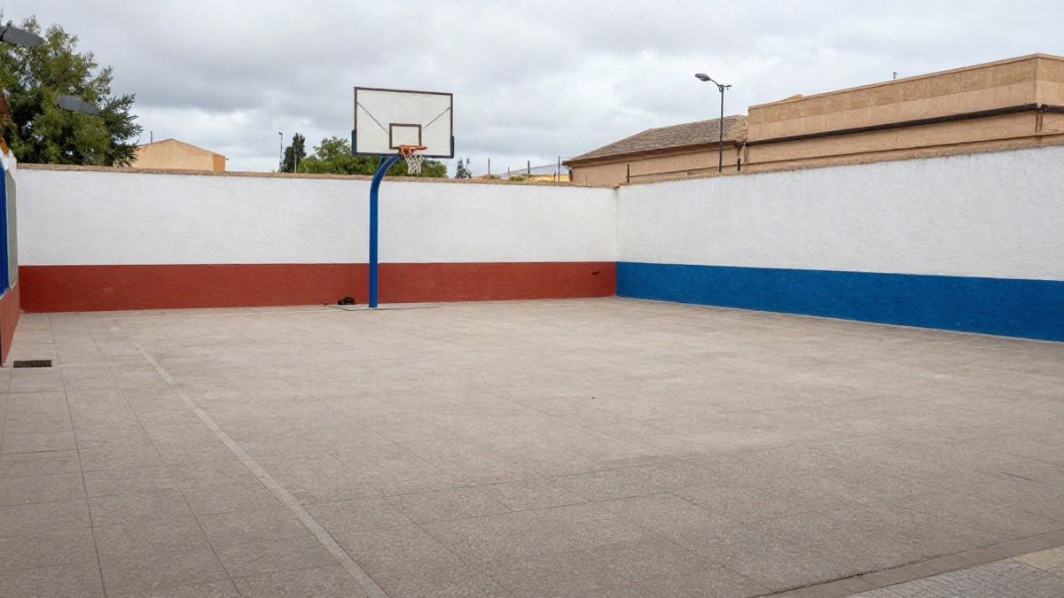 Imagen ilustrativa: patio de colegio con pavimento nuevo y una canasta de baloncesto al fondo, sin personas
