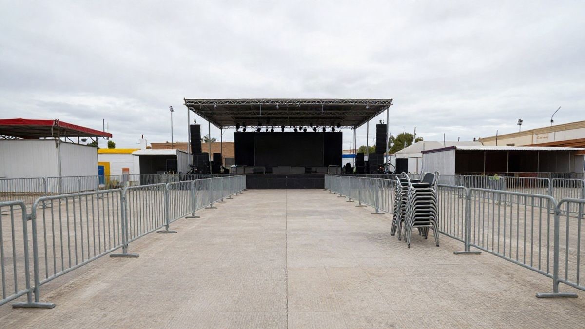 Illustrative image: empty outdoor stage with metal barriers and stacked chairs at a fairground