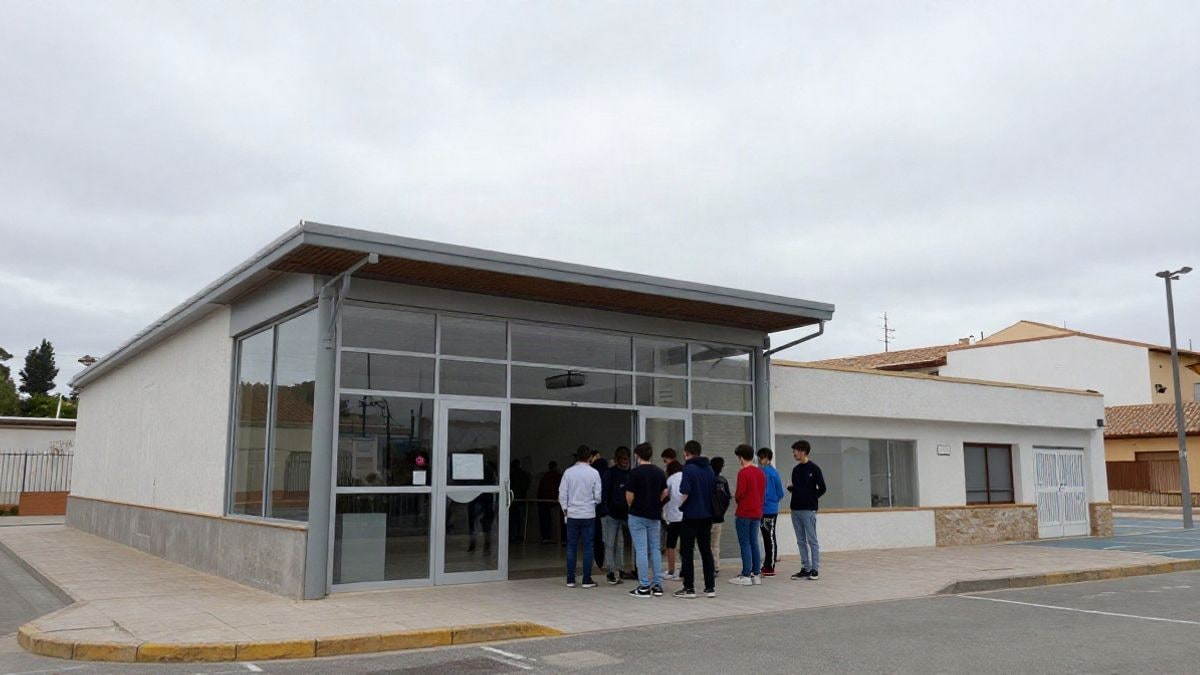 Imagen ilustrativa: edificio moderno de juventud con entrada de cristal y pista deportiva, con jóvenes de espaldas en la puerta.