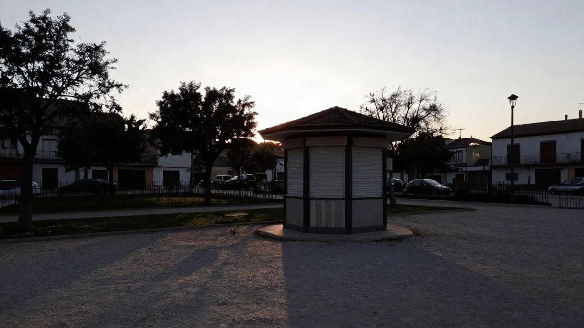 Imagen ilustrativa: un pequeño quiosco cerrado en un parque municipal al atardecer, con sombras largas en el camino