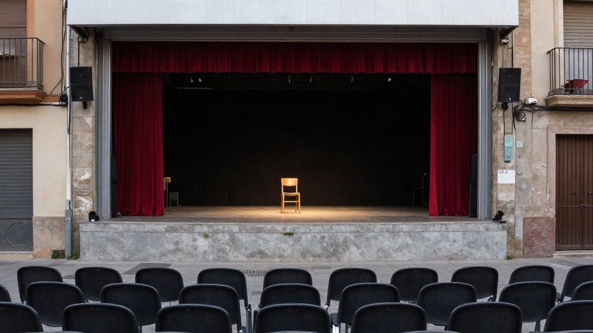 Imagen ilustrativa: escenario vacío de un pequeño teatro con una silla de madera bajo un foco y butacas en primer plano.