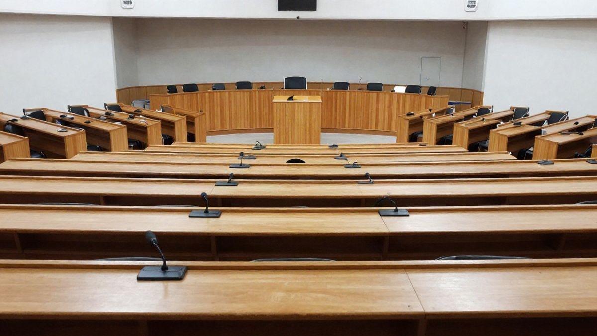 Imagen ilustrativa: sala de plenos vacía con escaños y atril, sin personas ni símbolos institucionales