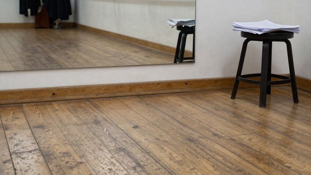 Imagen ilustrativa: suelo de madera desgastado de un estudio de danza con una barra y partituras sobre un taburete