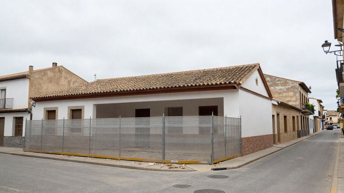 Imagen ilustrativa: calle de un municipio español con un edificio escolar en obras y valla de construcción