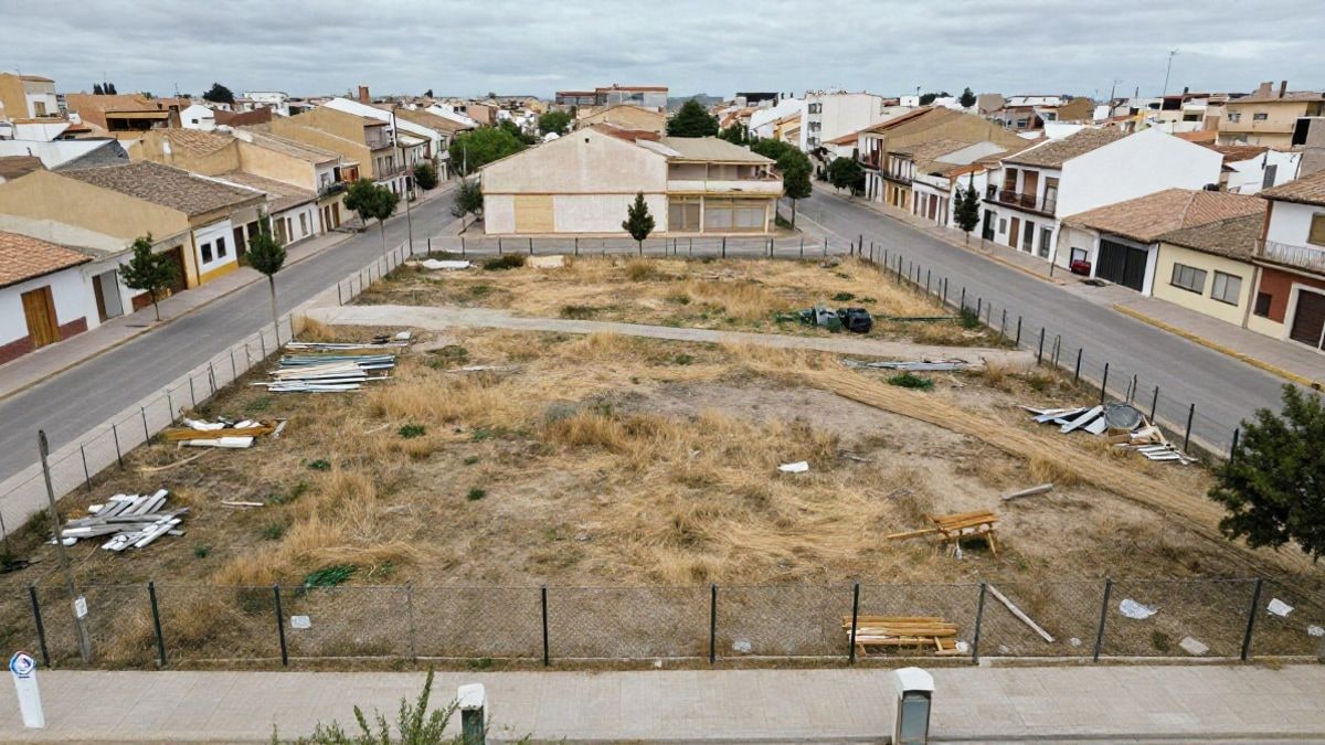 Illustrative image: aerial view of an empty urban plot with a metal fence and residential buildings around