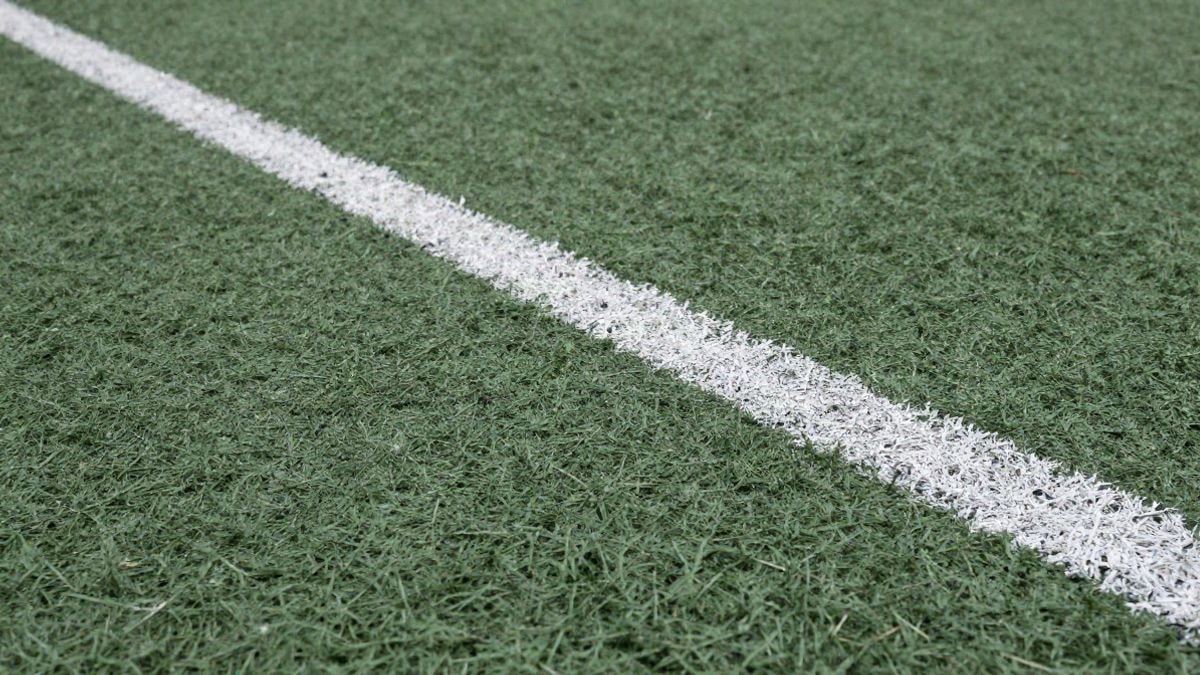Imagen ilustrativa: detalle de la textura de un césped artificial deportivo con línea blanca pintada