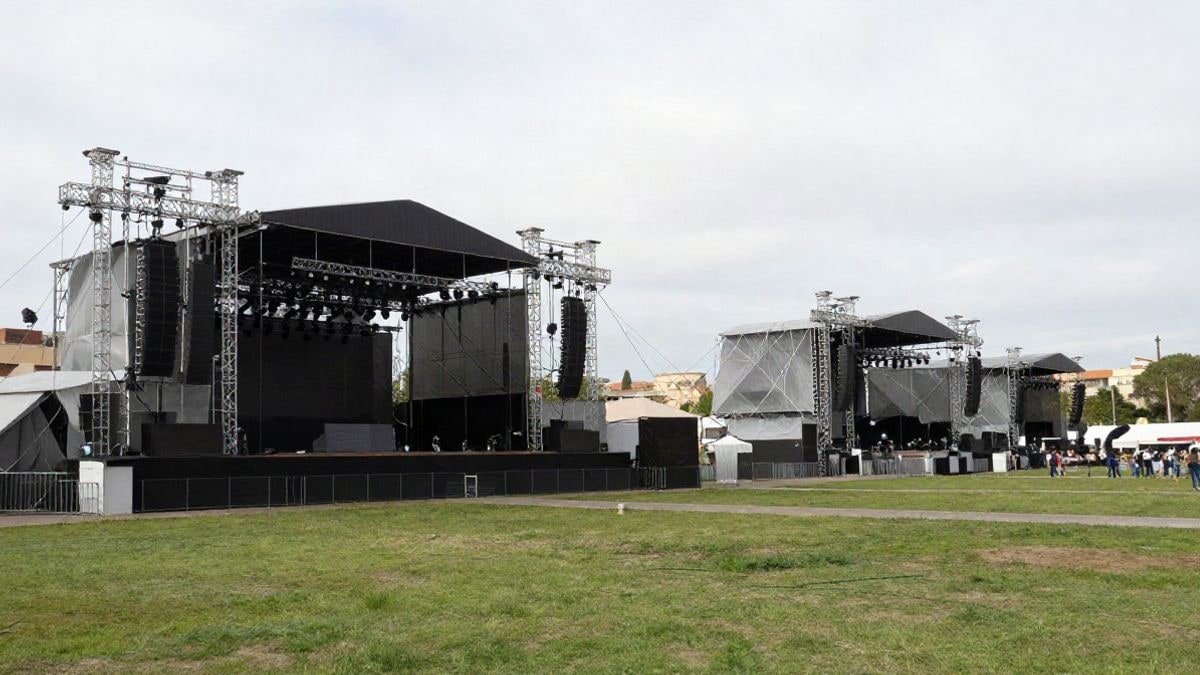 Imagen ilustrativa: gran angular de un escenario de festival al aire libre con líneas de estructura metálica y césped, sin público