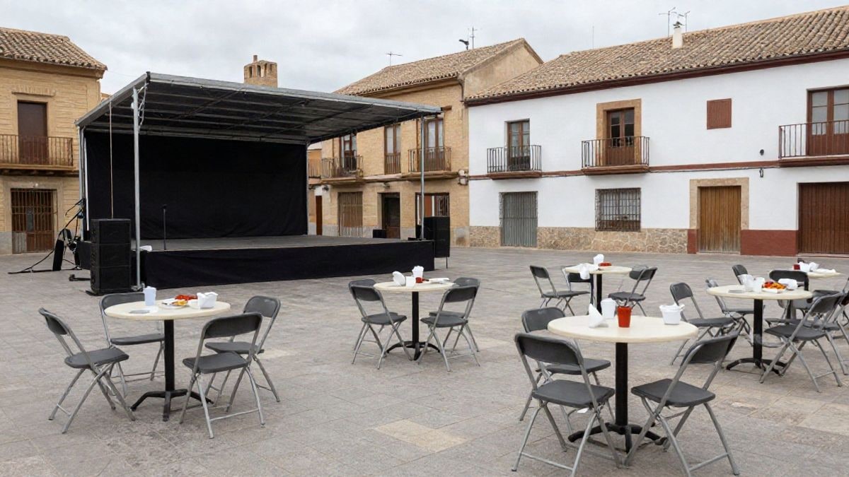 Imagen ilustrativa: plaza de un municipio español preparada para las fiestas, con escenario y sillas plegables