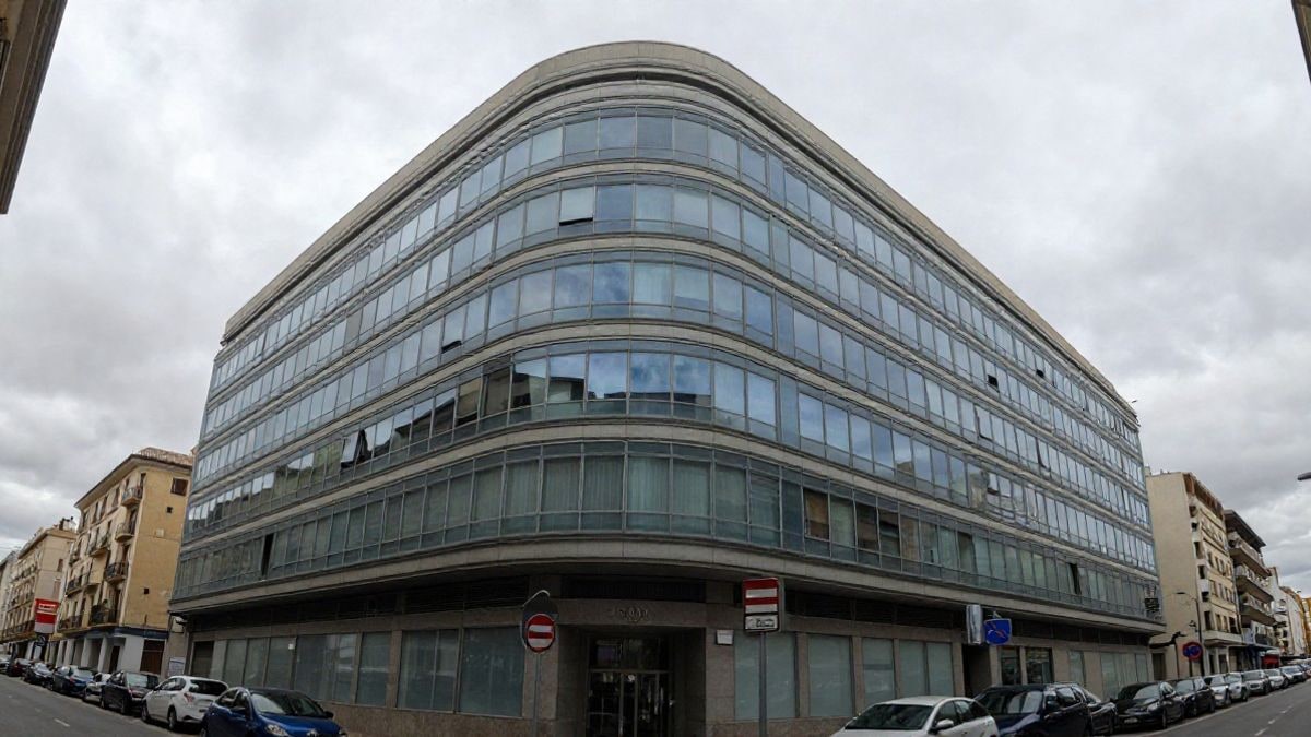 Illustrative image: low angle of a modern office building with a glass facade under a cloudy sky