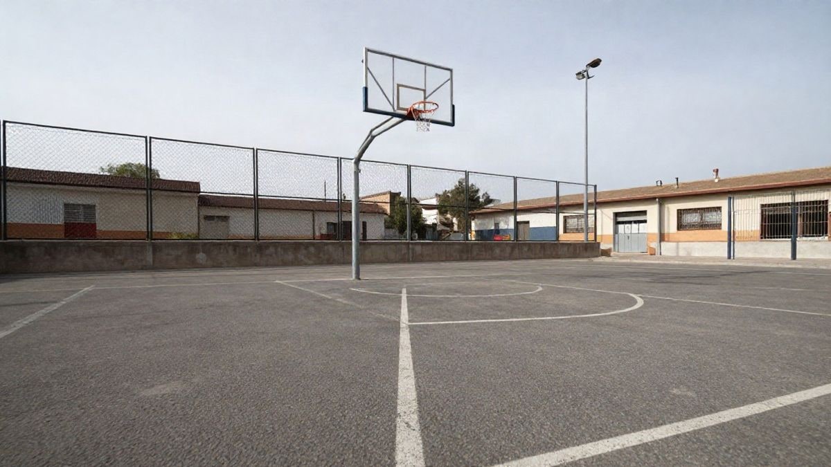 Imagen ilustrativa: patio escolar vacío con líneas pintadas en el suelo y una canasta de baloncesto, visto desde un ángulo bajo