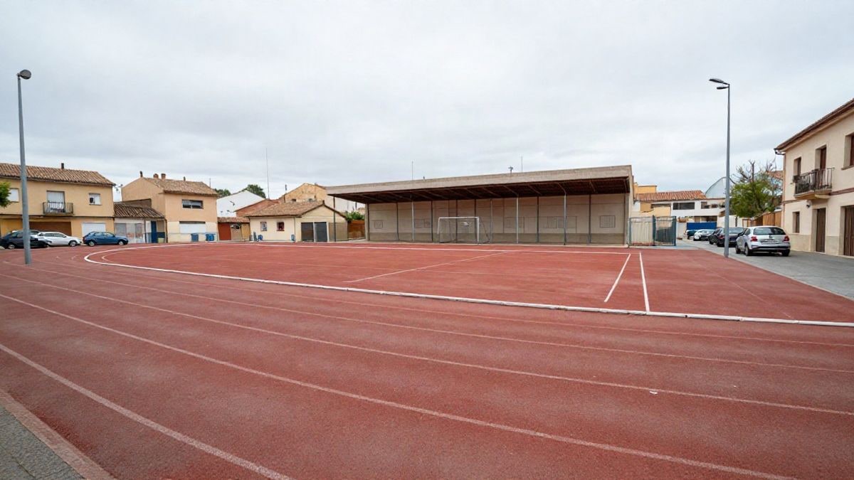 Imagen ilustrativa: exterior de un complejo deportivo municipal en un día nublado, con pista de atletismo y edificio polideportivo de fondo.