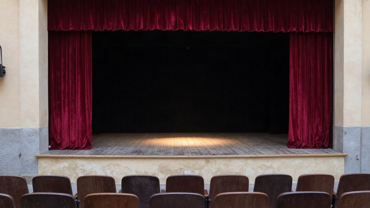 Imagen ilustrativa: escenario de un teatro pequeño con cortinas rojas y butacas vacías