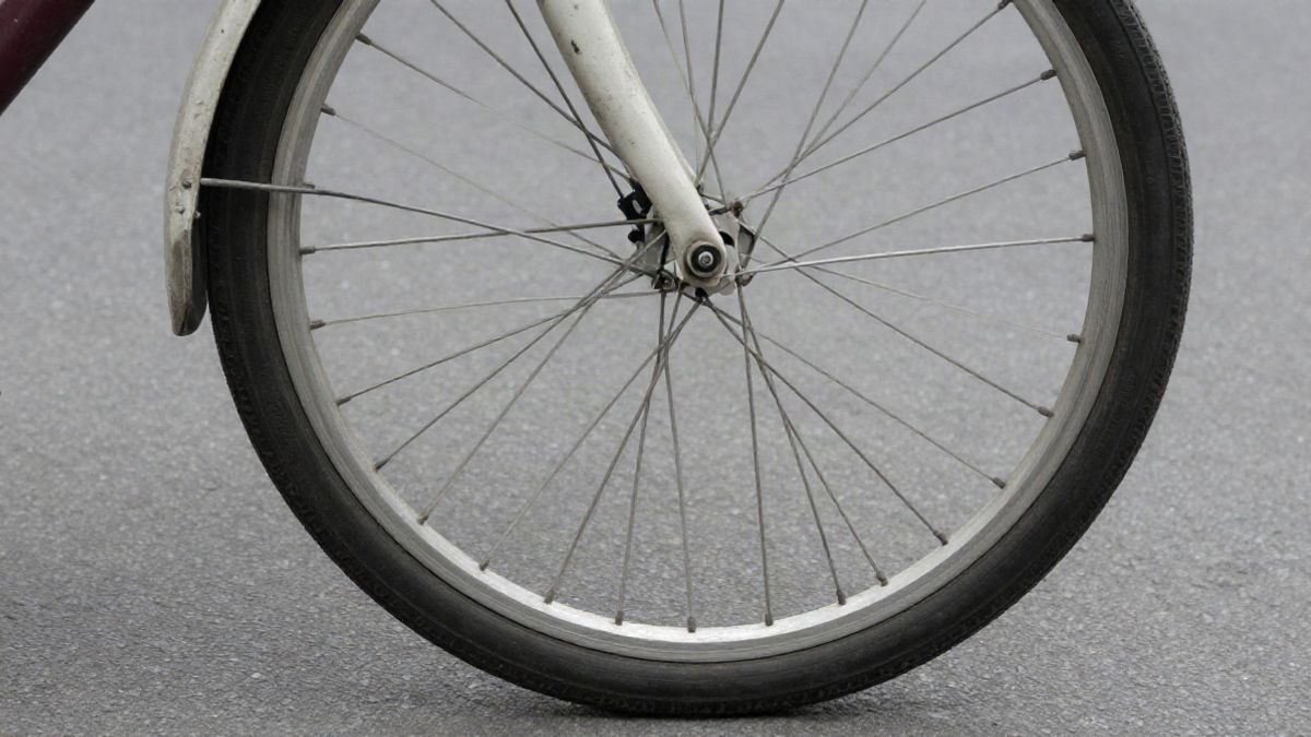 Imagen ilustrativa: detalle de una rueda de bicicleta y un casco infantil sobre el asfalto