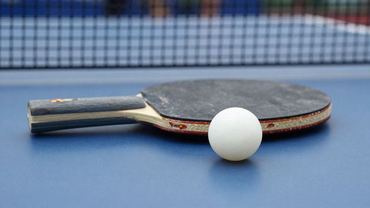 Imagen ilustrativa: primer plano de una pala y una pelota de ping pong sobre una mesa azul con la red al fondo