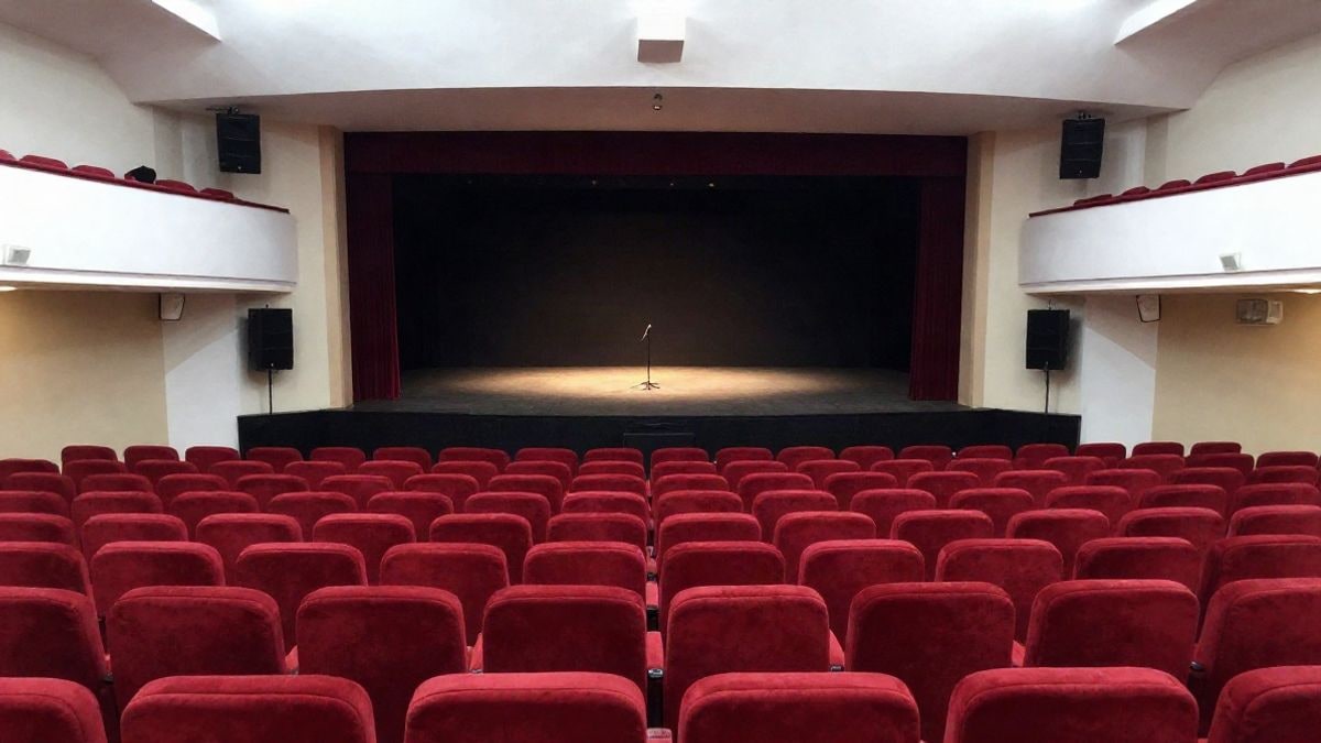 Imagen ilustrativa: interior de un teatro con butacas rojas y un escenario iluminado con focos, sin personas