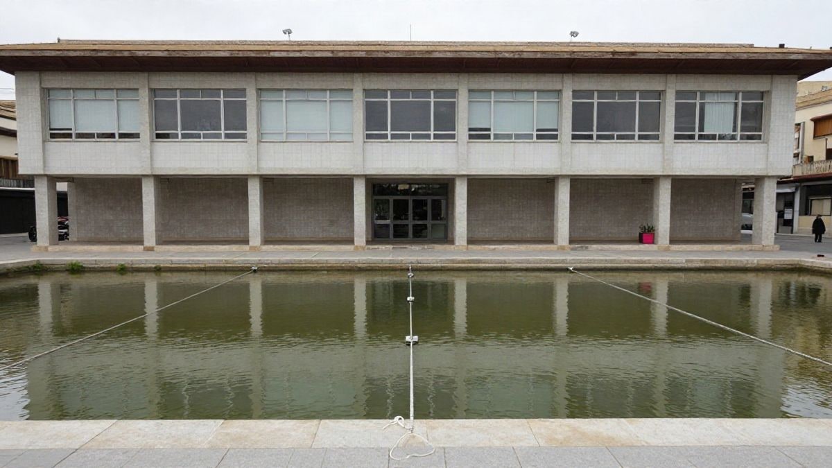 Imagen ilustrativa: piscina cubierta municipal vacía vista desde la grada, con las calles de agua y luz plana de día