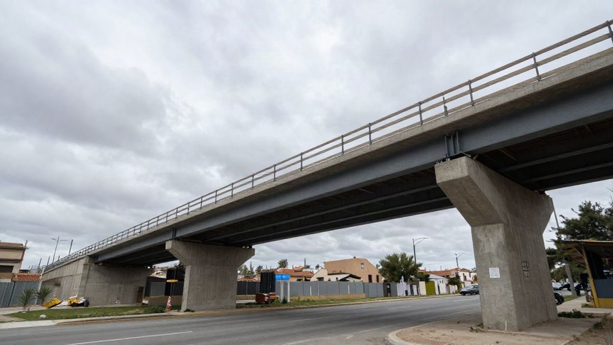 Imagen ilustrativa: pasarela peatonal en construcción sobre una carretera suburbana bajo un cielo nublado
