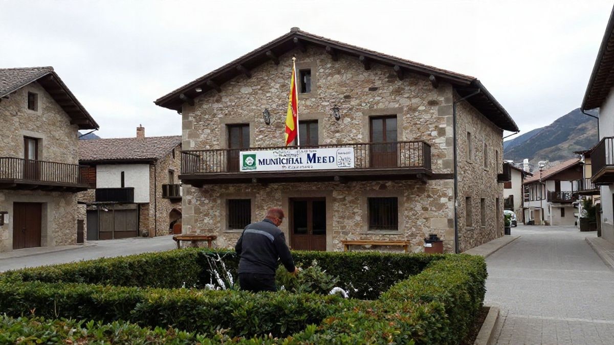 Illustrative image: a stone town hall building in a village in the Madrid mountains, with a gardener working in the background.
