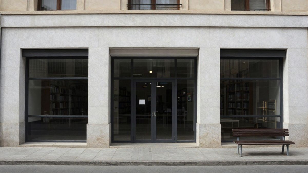 Imagen ilustrativa: fachada sencilla de una biblioteca pública vista desde la acera, con líneas que convergen y luz de día nublado
