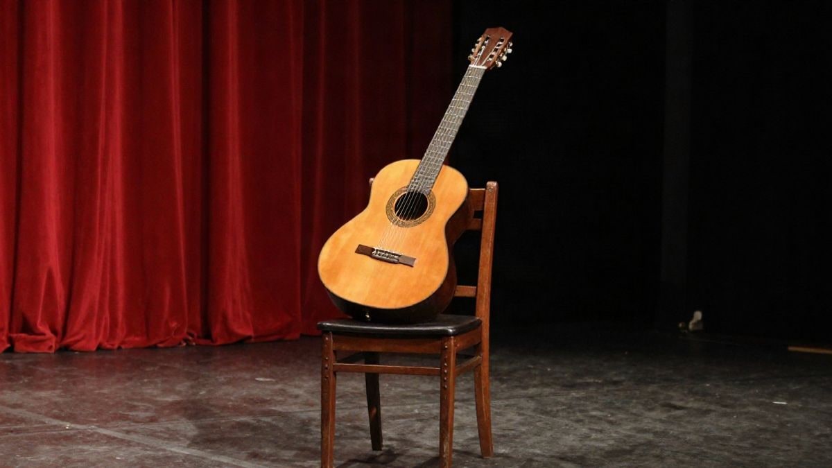Imagen ilustrativa: una guitarra flamenca sobre una silla en un escenario con focos y telón rojo de fondo
