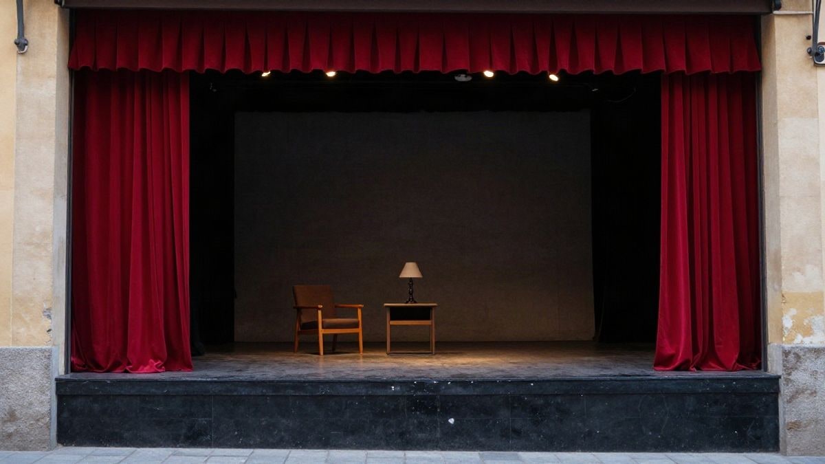 Imagen ilustrativa: un escenario teatral vacío con un sillón y una mesita de noche bajo focos cálidos.