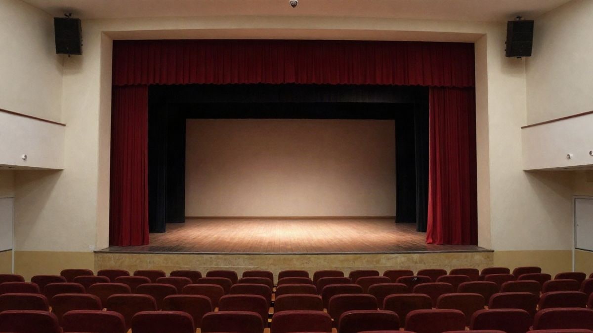 Imagen ilustrativa: un escenario teatral con cortinas rojas y un foco de luz, visto desde la platea vacía.